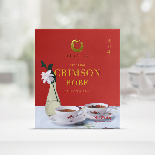 TEASPEC CRIMSON ROBE Da Hong Pao Chinese Loose Leaf Oolong Tea box with a net weight of 80g, comes in 8g Sachets x 10 per box. The front of the box design is a deep carmine color with a light blue soft floral-patterned tablecloth that has slim neck tall teardrop shaped vase with one white rose flower. Two white floral themed porcelain teacups in front on saucers. The Chinese name of the tea is 大红袍