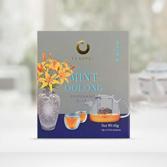 TEASPEC OOLONG MINT Peppermint & Qi Lan Chinese Loose Leaf Oolong Tea and peppermint leaves box with a net weight of 80g, comes in 8g Sachets x 10 per box. The front of the box design is a light stone-gray texture color with a navy tablecloth that has a gray porcelain vase with tiger lily flowers, a Lazy Pour Glass Teapot and 2 sip easy double walled glass teacups. The Chinese name of the tea is 乌龙薄荷