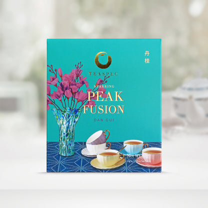 TEASPEC PEAK FUSION Dan Gui Chinese Loose Leaf Oolong Tea box with a net weight of 80g, comes in 8g Sachets x 10 per box. The front of the box design is a topaz color with a light navy tablecloth that has a glass vase with pink flowers and some white, baby blue, yellow and pink colored porcelain teacups with gold handles on it. The Chinese name of the tea is 丹桂