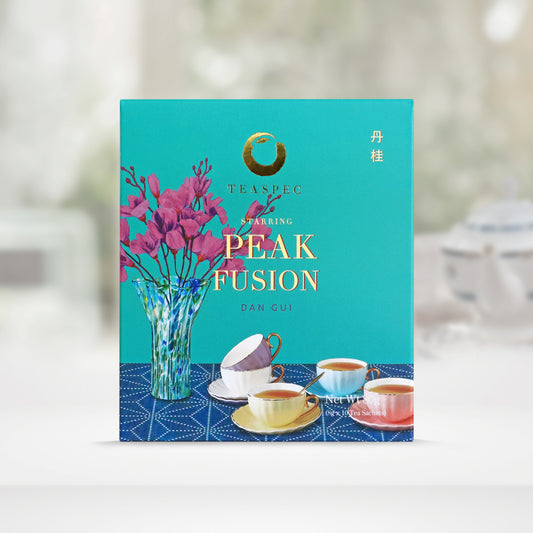 TEASPEC PEAK FUSION Dan Gui Chinese Loose Leaf Oolong Tea box with a net weight of 80g, comes in 8g Sachets x 10 per box. The front of the box design is a topaz color with a light navy tablecloth that has a glass vase with pink flowers and some white, baby blue, yellow and pink colored porcelain teacups with gold handles on it. The Chinese name of the tea is 丹桂