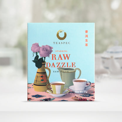 TEASPEC RAW DAZZLE Aged Raw Pu'er Chinese Loose Leaf Pu'er Tea box with a net weight of 50g, comes in 5g Sachets x 10 per box. The front of the box design is a powder blue color with a pink floral-patterned tablecloth that has a jug shaped rustic south American style vase with soft pink rose flowers. A tall light green-gray porcelain teapot with a tall handle and two white porcelain teacups in front on saucers. The Chinese name of the tea is 生普洱