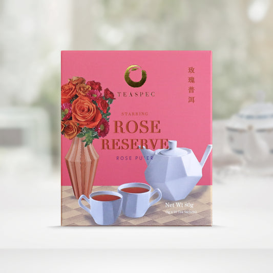 TEASPEC ROSE RESERVE Rose Pu'er  Chinese Loose Leaf Pu'er Tea box with a net weight of 80g, comes in 8g Sachets x 10 per box. The front of the box design is a pink rose color with a beige square geometric patterned tablecloth that has a designer vertical striped vase with various flowers, mainly roses. A designer white porcelain teapot with a unique handle and 2 matching teacups in front. The Chinese name of the tea is 玫瑰普洱
