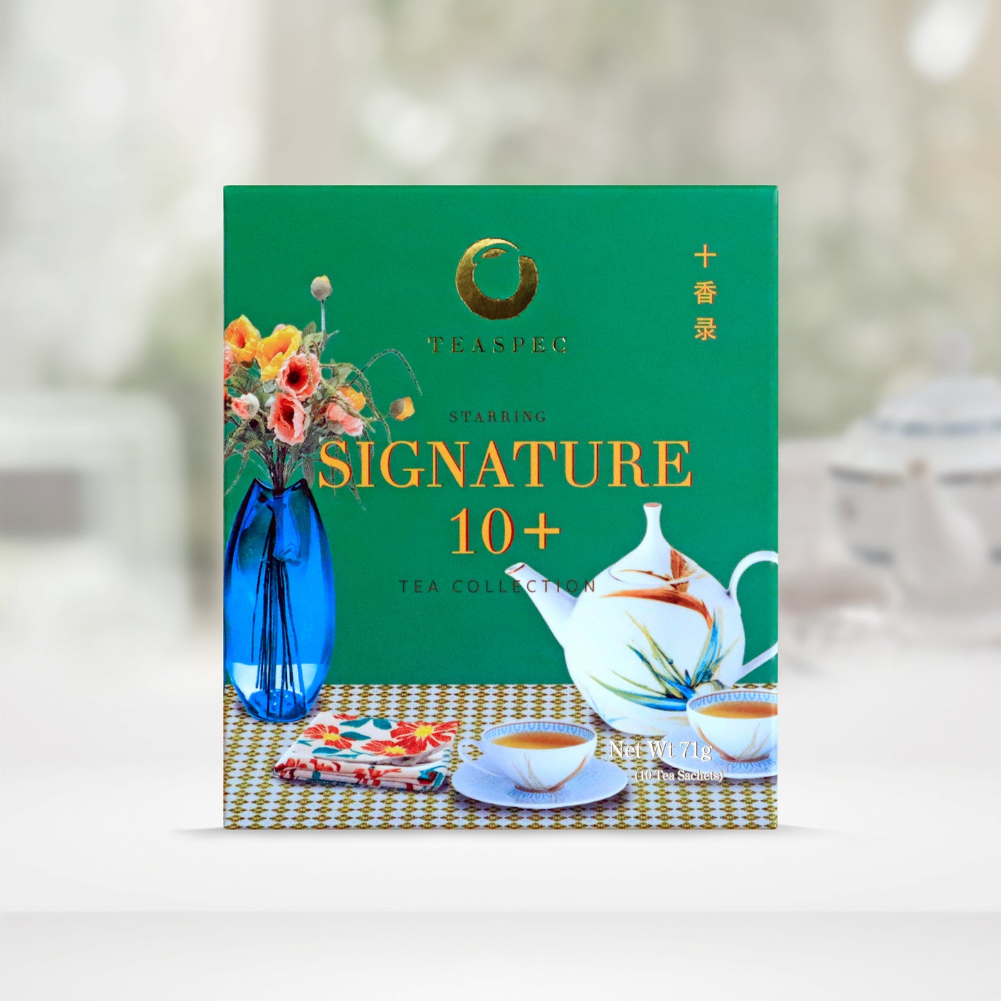 Signature 10 Tea Collection Pure Loose Leaf Chinese teas in a green box with a tabletop design that has a blue vase with various flowers and a floral rounded porcelain teapot with small matching teacups with saucers and a floral tea towel cloth on a yellow & white squared pattern tablecloth.