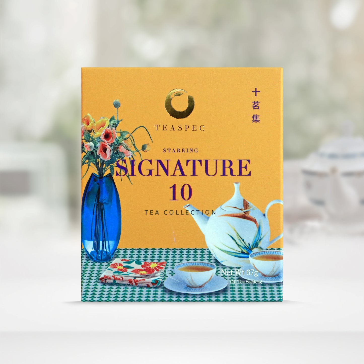 Signature 10 Tea Collection Pure Loose Leaf Chinese teas in a yellow box with a tabletop design that has a blue vase with various flowers and a floral rounded porcelain teapot with small matching teacups with saucers and a floral tea towel cloth on a green & white squared pattern tablecloth.