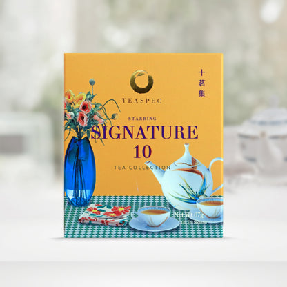 Signature 10 Tea Collection Pure Loose Leaf Chinese teas in a yellow box with a tabletop design that has a blue vase with various flowers and a floral rounded porcelain teapot with small matching teacups with saucers and a floral tea towel cloth on a green & white squared pattern tablecloth.