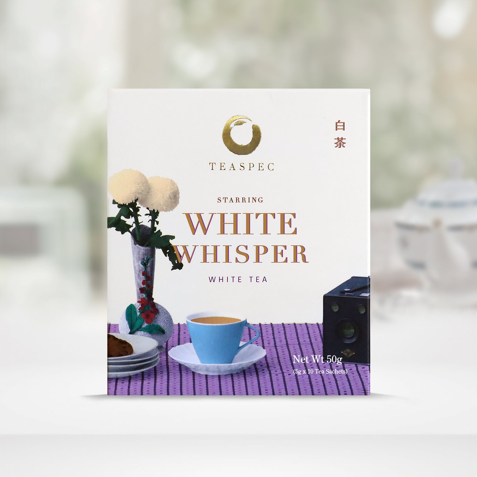 TEASPEC WHITE WHISPER White tea Shou Mei Tea box with a net weight of 50g, comes in 5g Sachets x 10 per box. The front of the box design is a floral white color with a striped light purple pattern tablecloth with slim neck floral porcelain vase with Chrysanthemum flowers. A portable retro device and a blue teacup and some plates. The Chinese name of the tea is 白茶